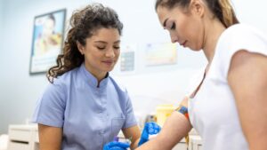 Medical technologist doing a blood draw services for patient. lab assistant with sterile rubber gloves taking blood sample from patient.