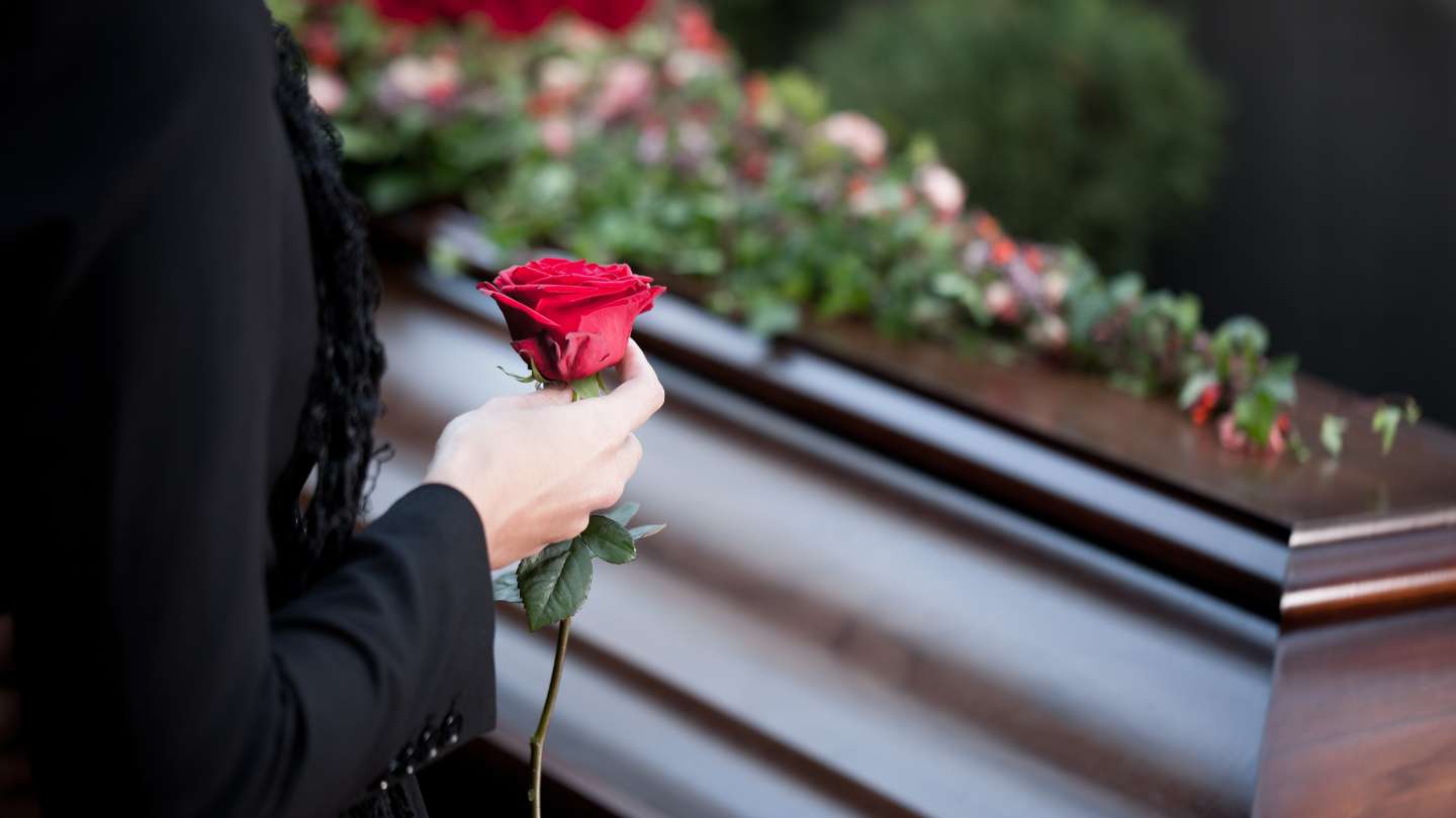 Mujer con una rosa en la mano en frente de un ataud antes de ser enterrado.