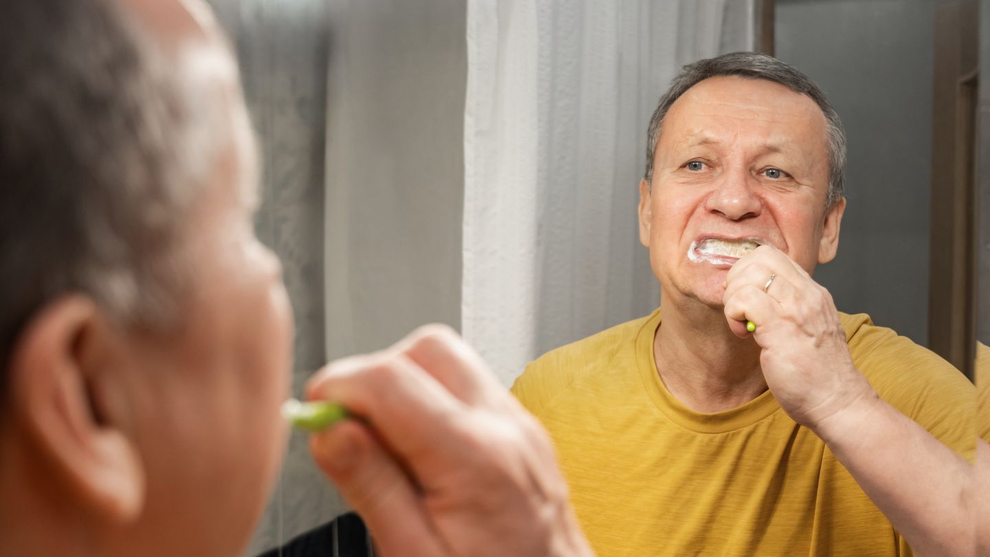 Señor cepillándose los dientes en frente del espejo.