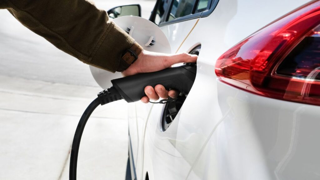 Mano enchufando el cargador a un coche eléctrico.