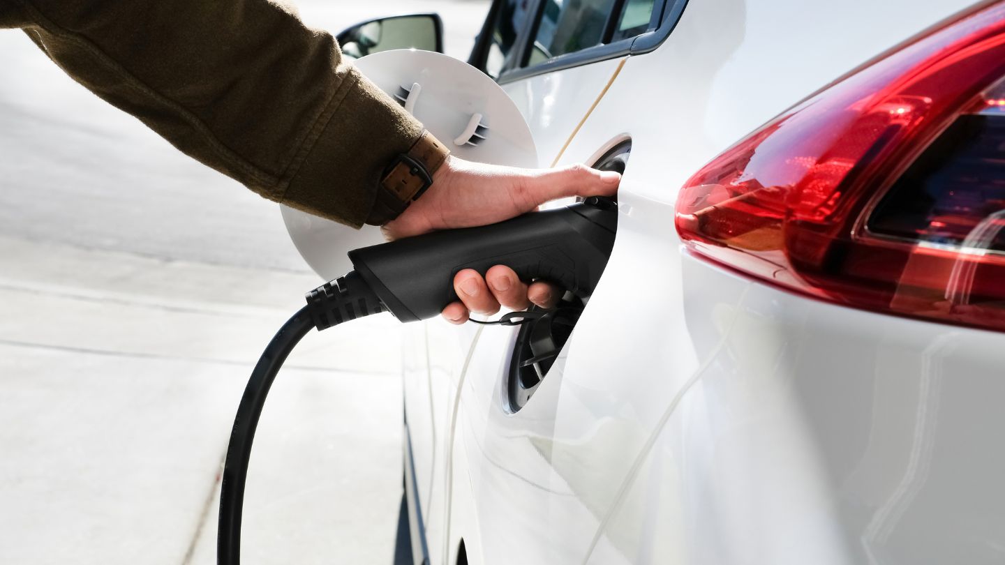 Mano enchufando el cargador a un coche eléctrico.